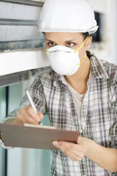 女建筑工人戴着面具 在剪贴板上写字 — 图库照片