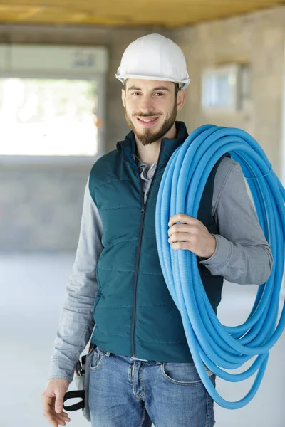 male tradesman with reel of blue pipe on his shoulder