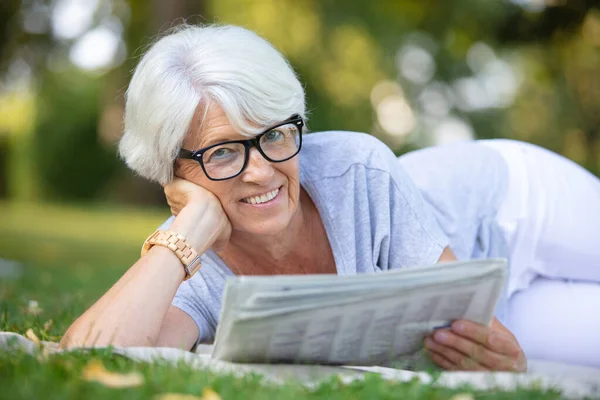 老年妇女躺在草地上看报纸 — 图库照片