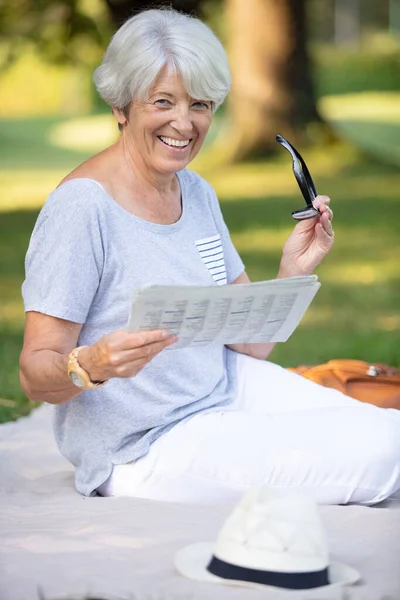 一位快乐的老年妇女一边看报纸一边笑 — 图库照片