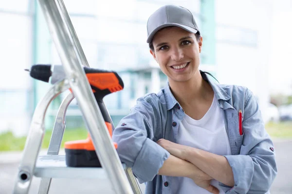 Fröhliche Frau Sitzt Mit Elektrobohrer Auf Trittleiter — Stockfoto