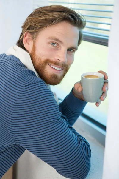 コーヒーを片手に窓の近くに座っている若い男の肖像画 — ストック写真