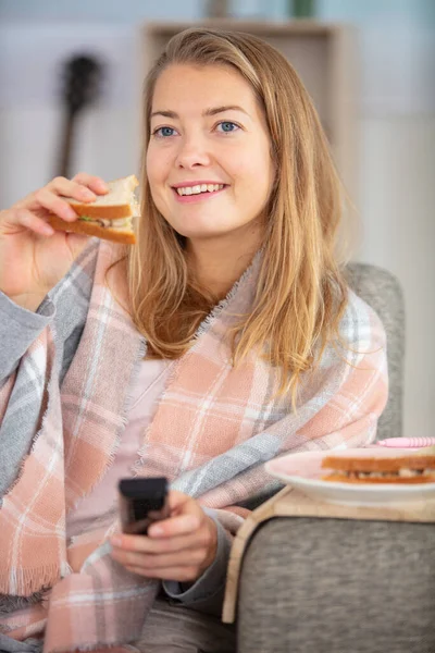 hungry woman holding a sandwich while watching tv
