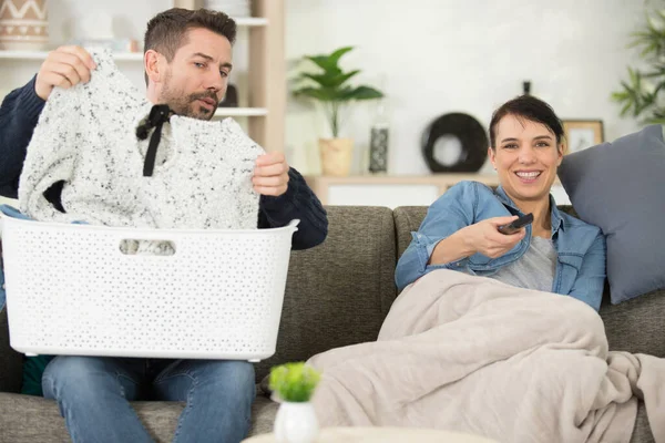Νοικοκυρά Βλέπει Τηλεόραση Ενώ Σύζυγος Πλένει Ρούχα — Φωτογραφία Αρχείου