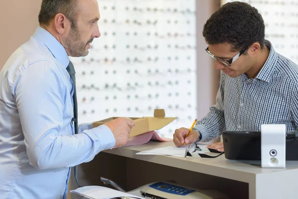 男性眼科医生和客户在柜台填写文书工作 — 图库照片