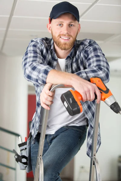 Glücklicher Männlicher Bauarbeiter Steht Mit Bohrmaschine Auf Leiter — Stockfoto
