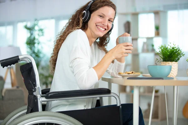 坐在轮椅上的年轻妇女吃早餐 戴耳机 — 图库照片