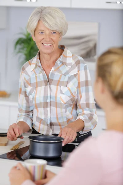 年上の笑顔の女性キッチンストーブの上でお湯を沸かす — ストック写真