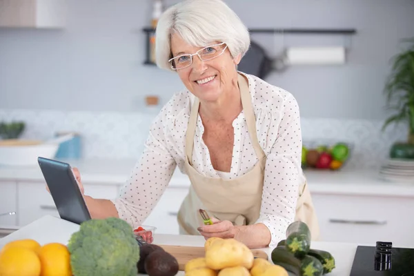 高齢の女性はタブレットでレシピの助けを借りて料理します — ストック写真