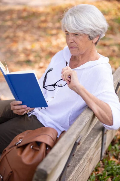 老年妇女在长椅上看书 — 图库照片