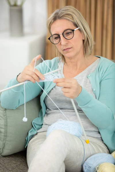 眼鏡をかけた女性がソファで編み物をしています — ストック写真