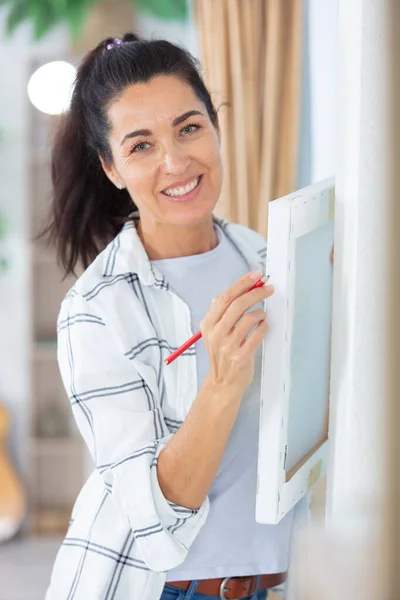 美しい女性が家の壁に絵を掛け — ストック写真