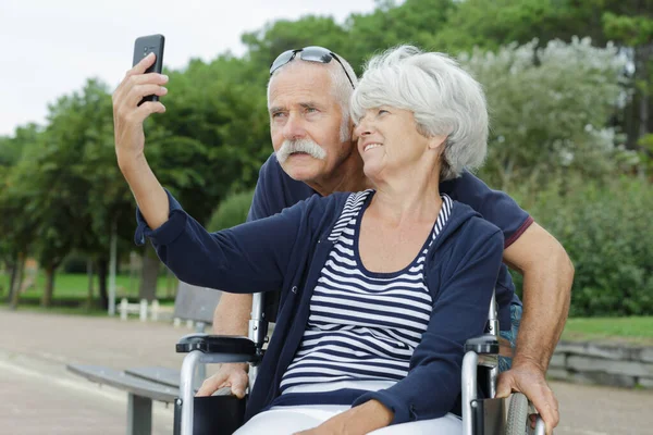 Parktaki Yaşlı Çift Tekerlekli Sandalyede Selfie Çeken Kadını Götürüyor — Stok fotoğraf