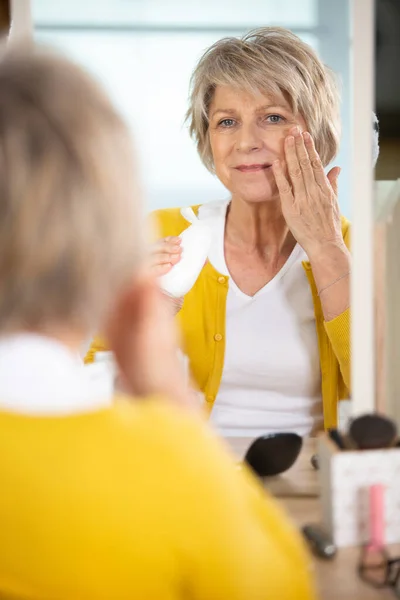 五十多岁的女士把护肤产品涂在脸上 — 图库照片