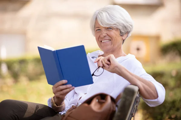Ηλικιωμένη Γυναίκα Καθόταν Στο Παγκάκι Διαβάζοντας Ένα Βιβλίο — Φωτογραφία Αρχείου