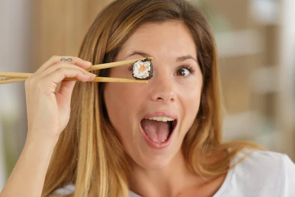 微笑的女人拿着寿司在眼睛前用筷子 — 图库照片