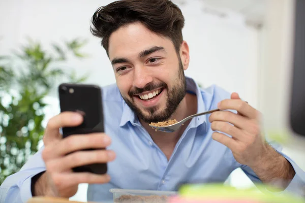 若いビジネスマンが昼飯を食べながら電話をチェックしている — ストック写真