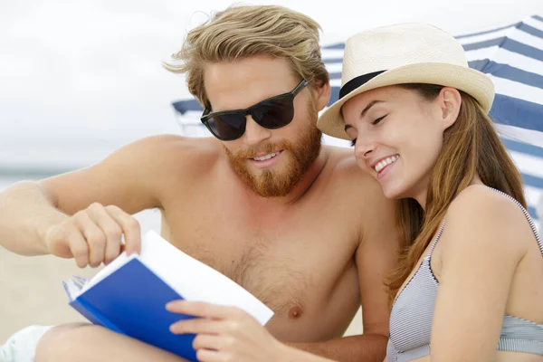ビーチで本を見て笑っている夫婦は — ストック写真