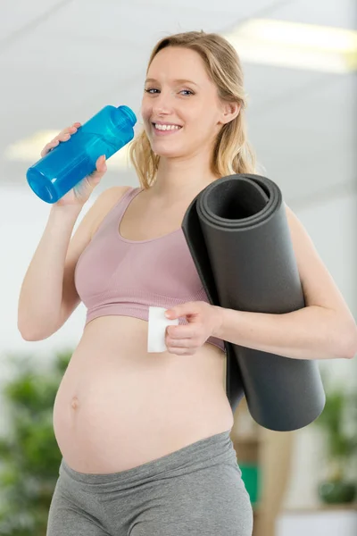 妊娠中の女性は運動マットと水のボトルを持って — ストック写真