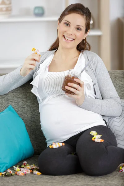 チョコレートを食べるのを楽しんで自宅で笑顔の妊婦 — ストック写真