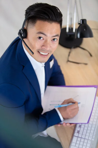 头戴耳机的亚裔男子坐在电脑桌前 — 图库照片