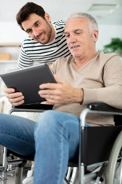 在轮椅上向年迈的父亲展示数码平板电脑的人 — 图库照片