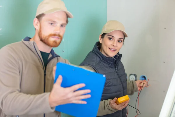男性と女性の電気技師がマルチメーターで回路をテストし — ストック写真