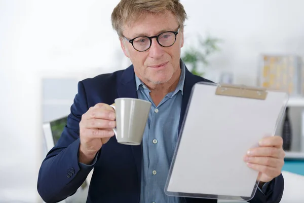 Mann Checkt Klemmbrett Mit Kaffeebecher Auf Heimischen Tisch — Stockfoto