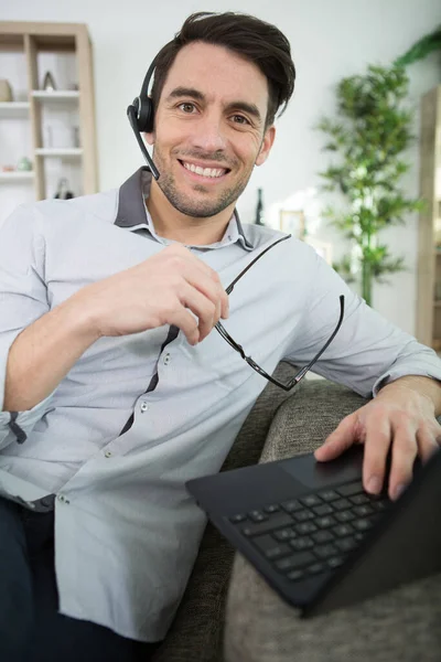 头戴耳机的男人坐在沙发上 拿着笔记本电脑 — 图库照片