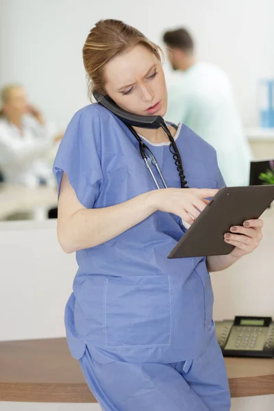 护士在阅读剪贴板上的文档时 用智能手机交谈 — 图库照片