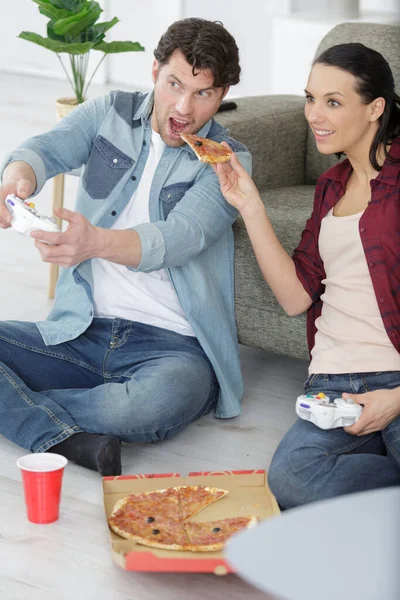 夫妻在家里玩电子游戏的同时吃着美味的披萨 — 图库照片