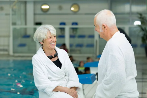 年长夫妇穿著浴衣在室内游泳池边笑 — 图库照片