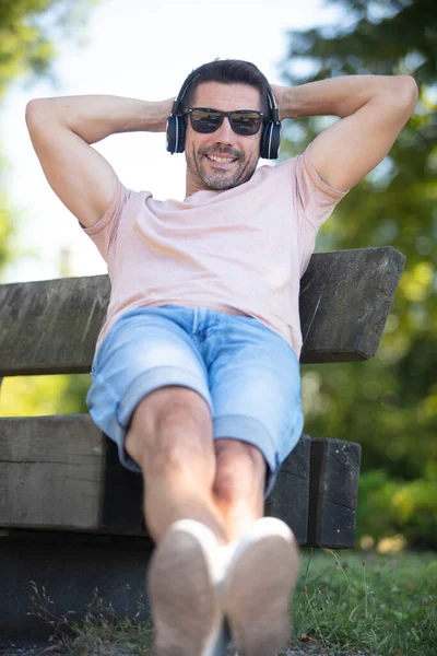 Χαλαρός Άνθρωπος Ακούει Μουσική Χρησιμοποιώντας Ακουστικά Εξωτερικούς Χώρους Στον Πάγκο — Φωτογραφία Αρχείου