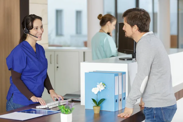 Paziente Guardando Receptionist Femminile Utilizzando Cuffie Telefono Alla Reception — Foto Stock