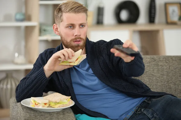 Άνθρωπος Αλλαγή Τηλεοπτικό Κανάλι Τηλεχειριστήριο Ενώ Τρώει Σάντουιτς — Φωτογραφία Αρχείου