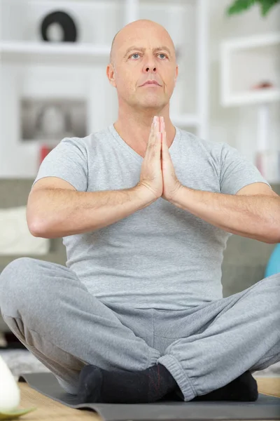 放松成熟的男人坐在瑜伽垫上在家里 — 图库照片