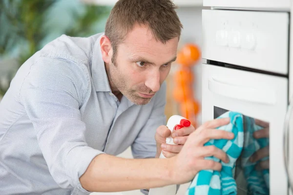 男人在烤箱上喷洒杀虫剂 — 图库照片