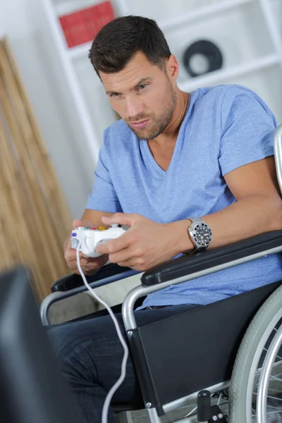 坐在轮椅上的男人在家里玩电子游戏 — 图库照片