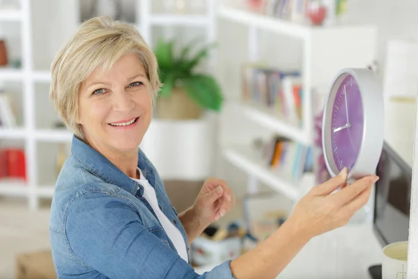 快乐的老年妇女把挂钟保持在室内 — 图库照片