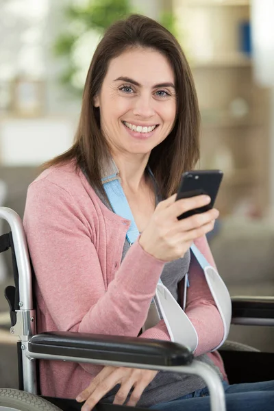 woman in wheelchair with arm in a sling using smartphone