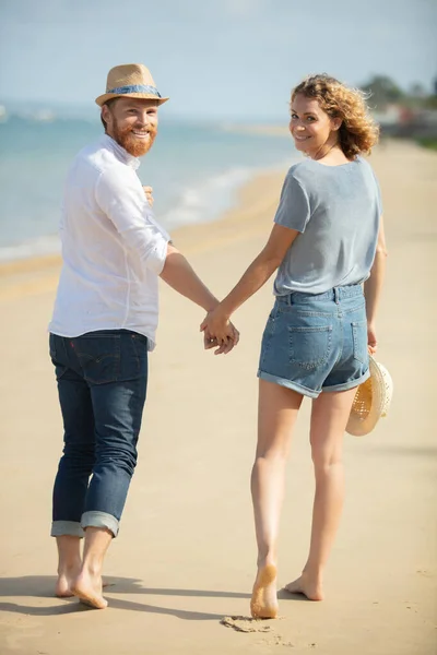 ビーチで手をつないで歩くカップルは — ストック写真