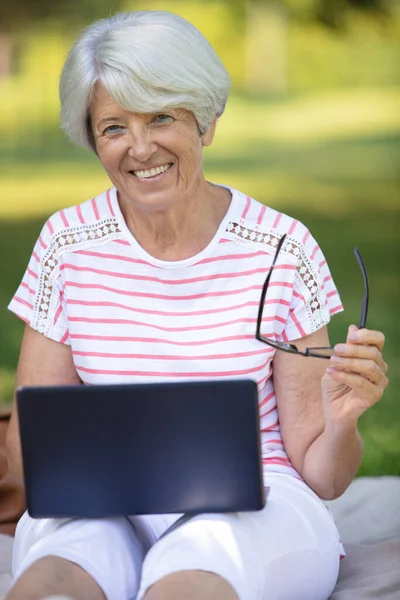 一位带着笔记本电脑坐在户外的老年妇女美丽的微笑 — 图库照片