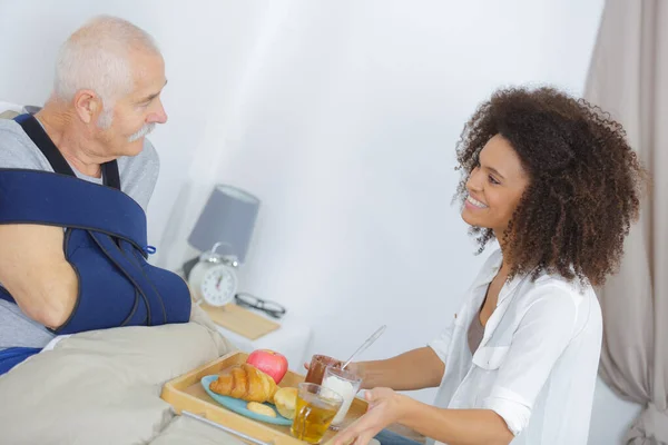 Glimlachende Vrouwelijke Verpleegster Serveert Ontbijt Aan Senior Man — Stockfoto