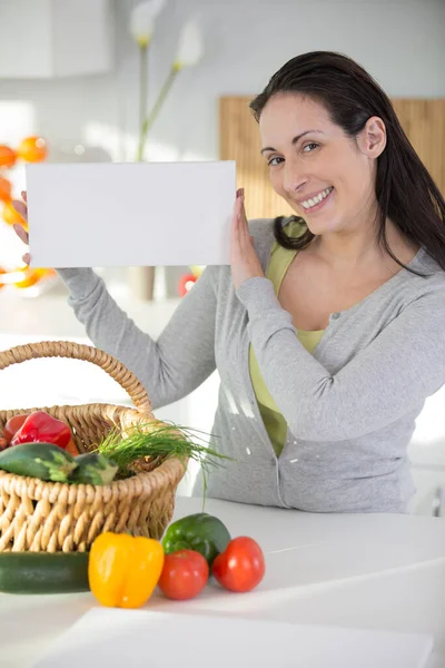 厨房里拿着新鲜蔬菜的女人拿着空白牌子 — 图库照片