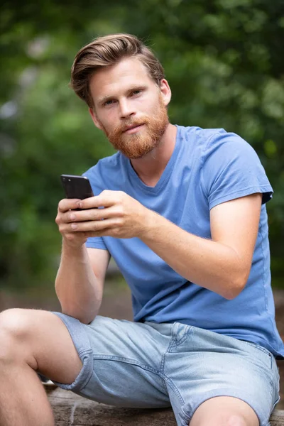 Homem Senta Tronco Árvore Floresta Usando Telefone Celular — Fotografia de Stock