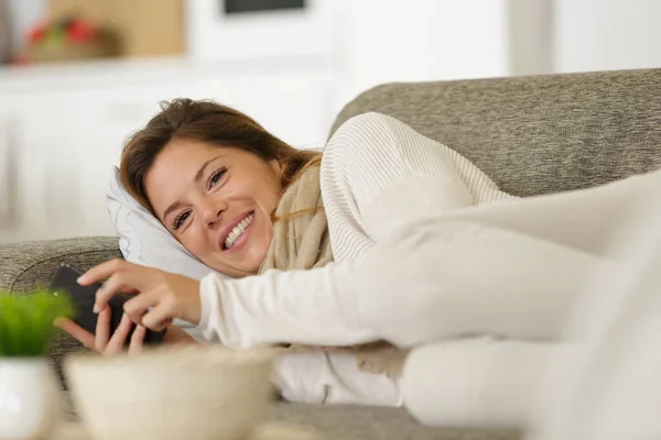 女人用智能手机躺在沙发上 — 图库照片