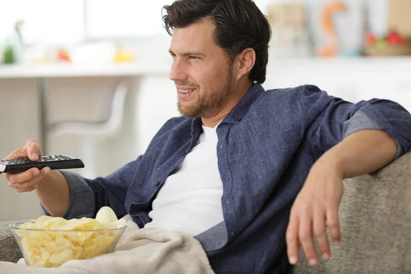 男人拿着遥控器看电视 吃着薯片 — 图库照片