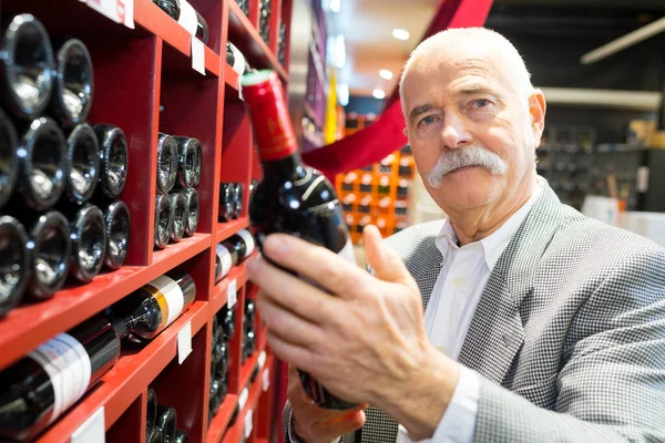 Starszy Mężczyzna Trzymający Butelkę Wina Sklepie Winami — Zdjęcie stockowe