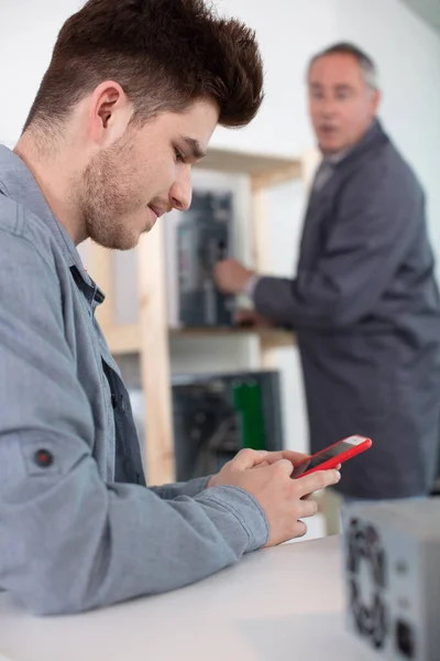 older colleague sees young man using smartphone while at work