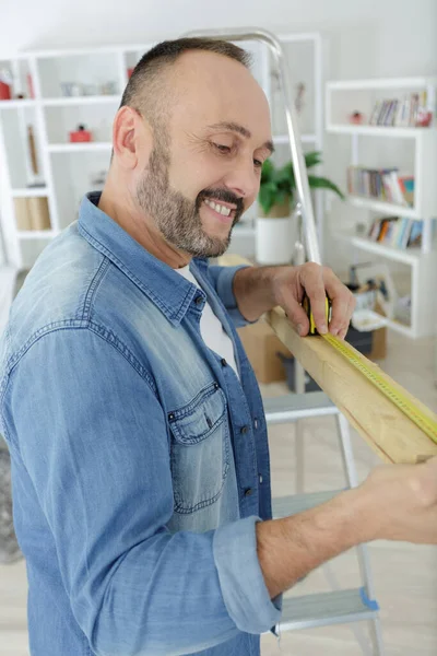 stock image man measuring wood piece for furniture assembling